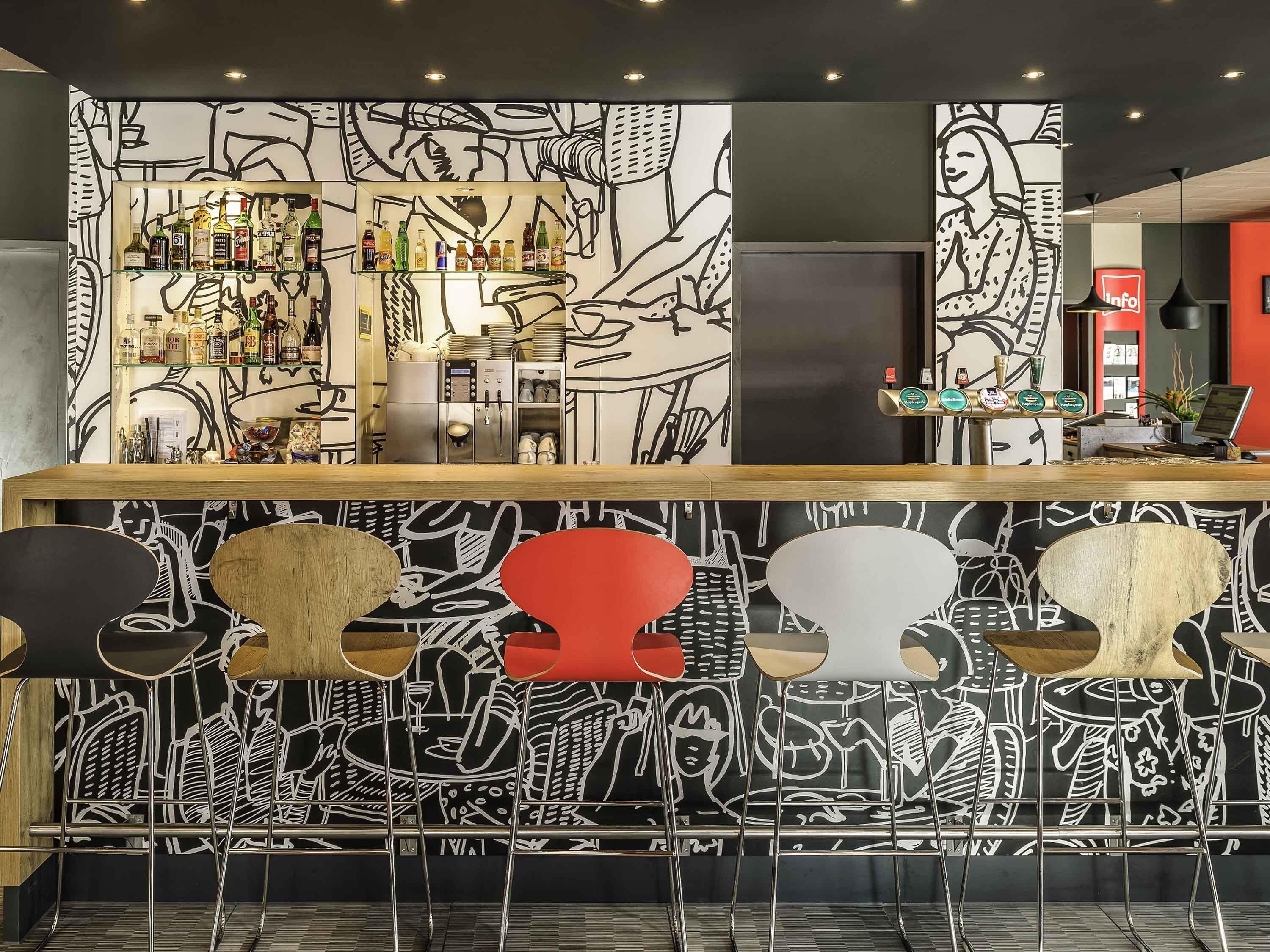 Una zona de bar con mostrador, estantes llenos de botellas y una pared con diseños abstractos.