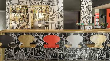 Una zona de bar con mostrador, estantes llenos de botellas y una pared con diseños abstractos.