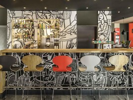 Una zona de bar con mostrador, estantes llenos de botellas y una pared con diseños abstractos.