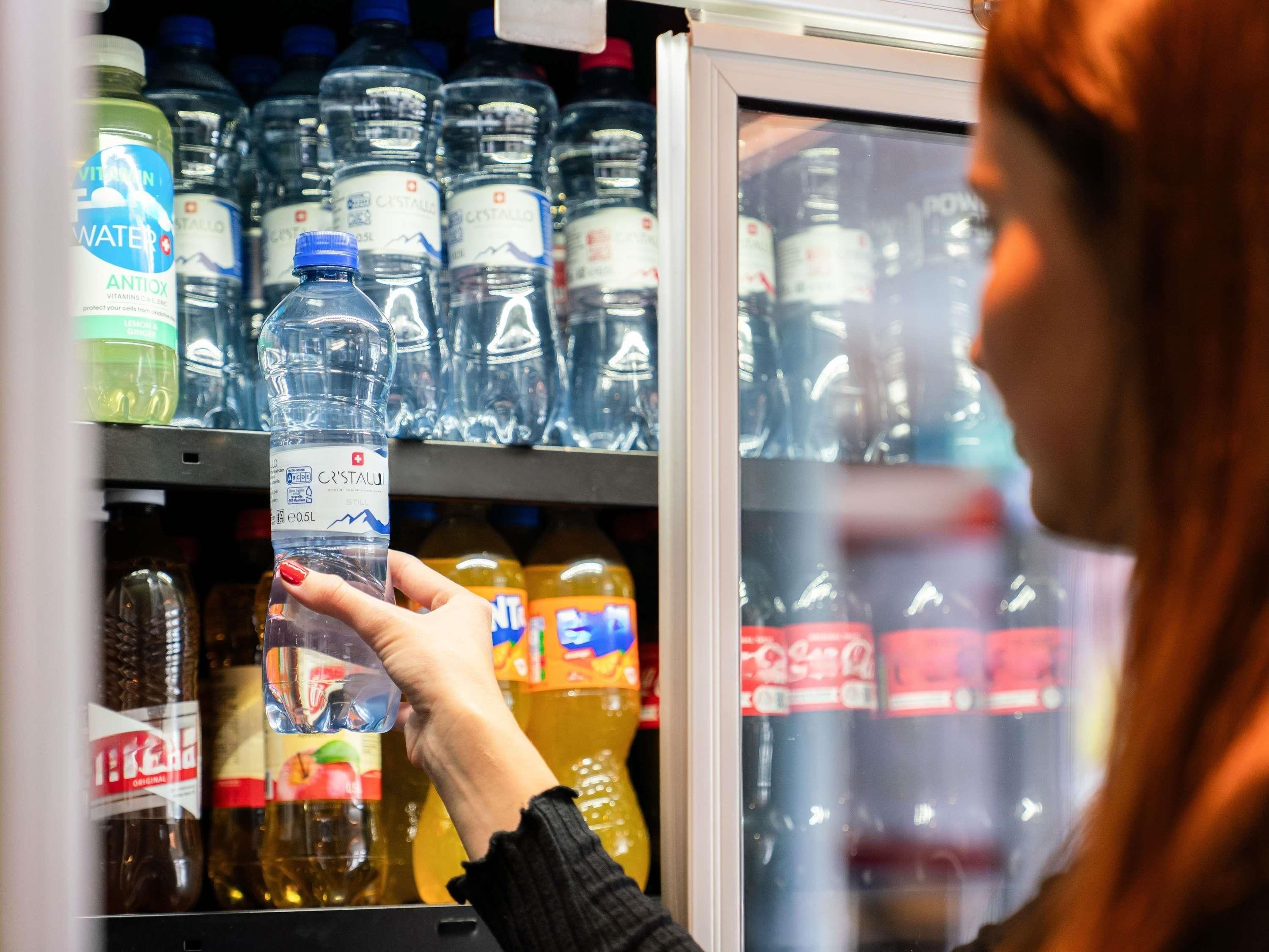 A person holding a bottle of water in a refrigerated section of a store.