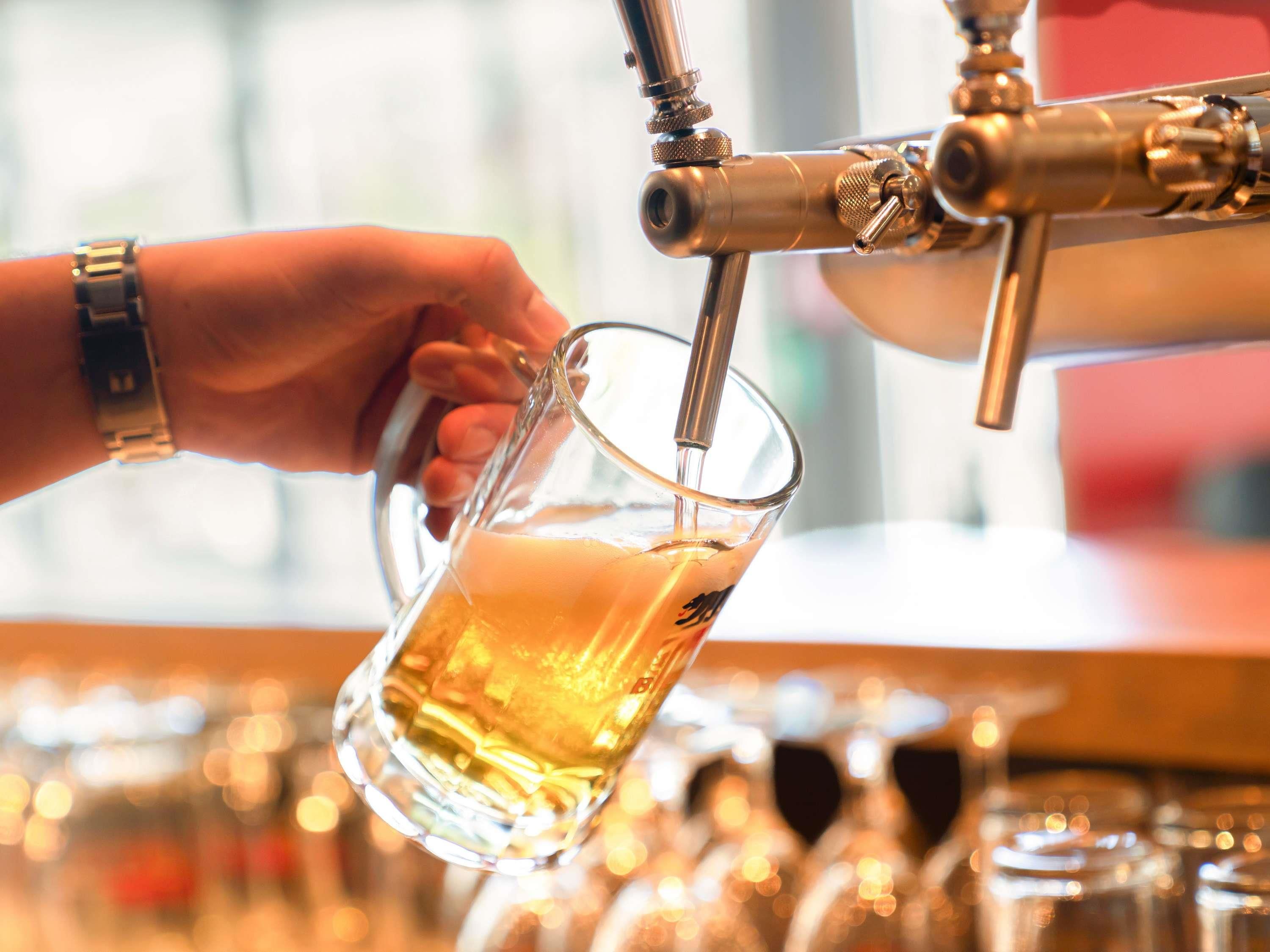 Eine Hand hält ein Glas unter einem Wasserhahn, vermutlich in einer Bar.