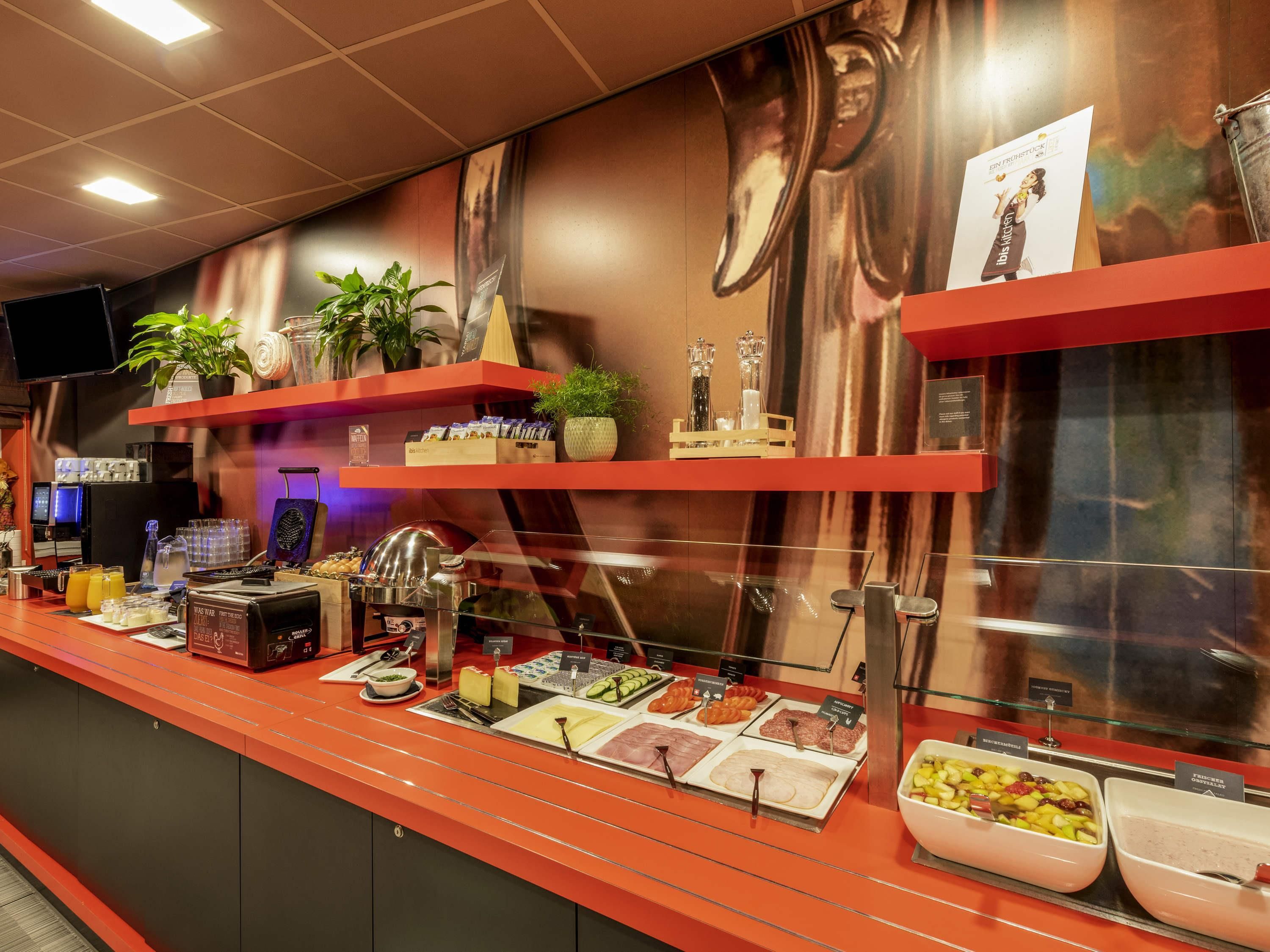 Una barra de desayuno con diferentes opciones de comida, una máquina de café y un televisor en la pared.