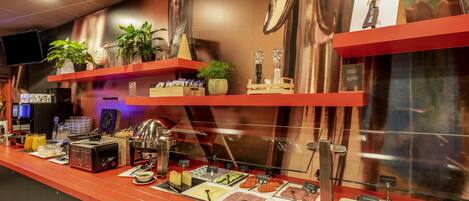 A breakfast bar with various food items, a coffee machine, and a television on the wall.