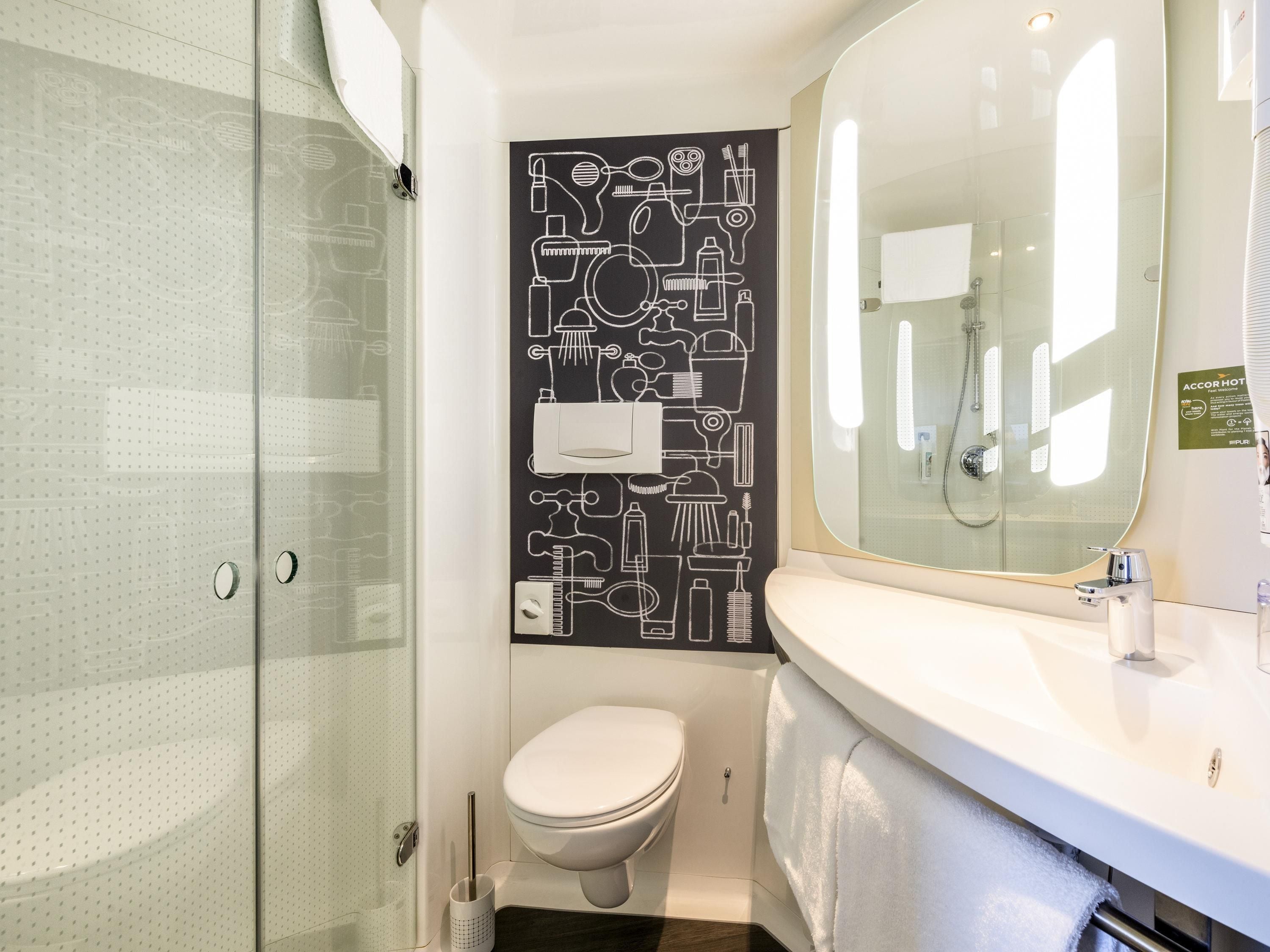 A modern bathroom with a glass shower enclosure, a white toilet, and a large mirror above a white sink.