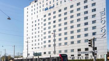 Un bâtiment d’hôtel moderne, avec une enseigne bien visible indiquant « hôtel ibis », une ligne de tramway et une enseigne indiquant un « espace restauration ».