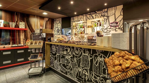 Een bakkerijbalie met gebak, een koffiemachine en een muur met zwart-wit illustraties.