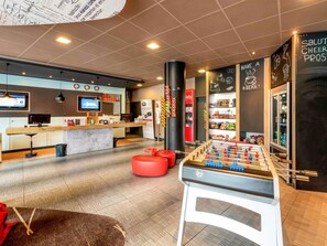 A modern lobby with a reception desk, a foosball table, and a bar area. - ibis Bern Expo (Bern)