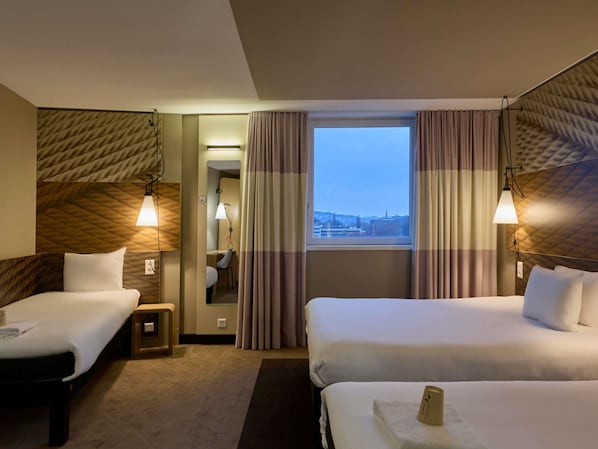 A hotel room with two beds, a desk, a chair, a window with curtains, and a city view.