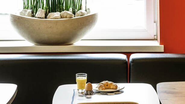 Un comedor con una mesa lista para el desayuno, incluyendo cruasanes y jugo de naranja, cerca de una ventana con vistas.