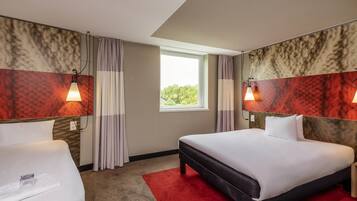 A hotel room with two beds, a red carpet, and a window with a view of greenery.