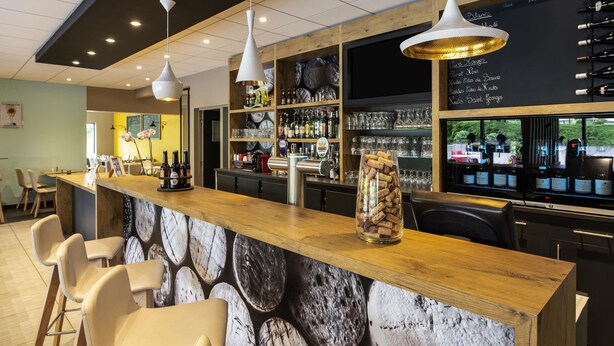 A bar area with a wooden counter, bar stools, hanging pendant lights, and a wine list on the wall. - ibis Nuits Saint Georges (Nuits-Saint-Georges)