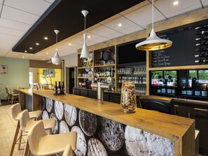 Un espace bar avec un comptoir en bois, des tabourets de bar, des luminaires suspendus et une carte des vins affichée au mur.