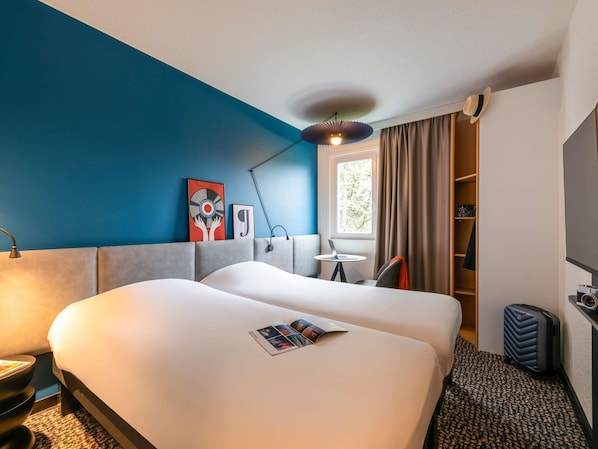 Une chambre d’hôtel avec un grand lit, un bureau, une chaise, une lampe, une fenêtre avec des rideaux et une bibliothèque.