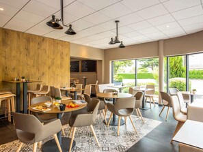 A modern cafe with round tables, chairs, and a menu board. - ibis Nuits Saint Georges (Nuits-Saint-Georges)