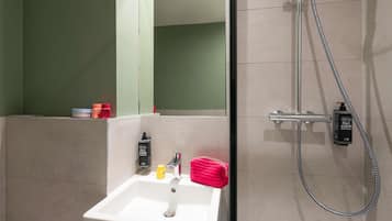 Un baño con lavamanos blanco, un espejo y una ducha con cabezal de ducha manual.