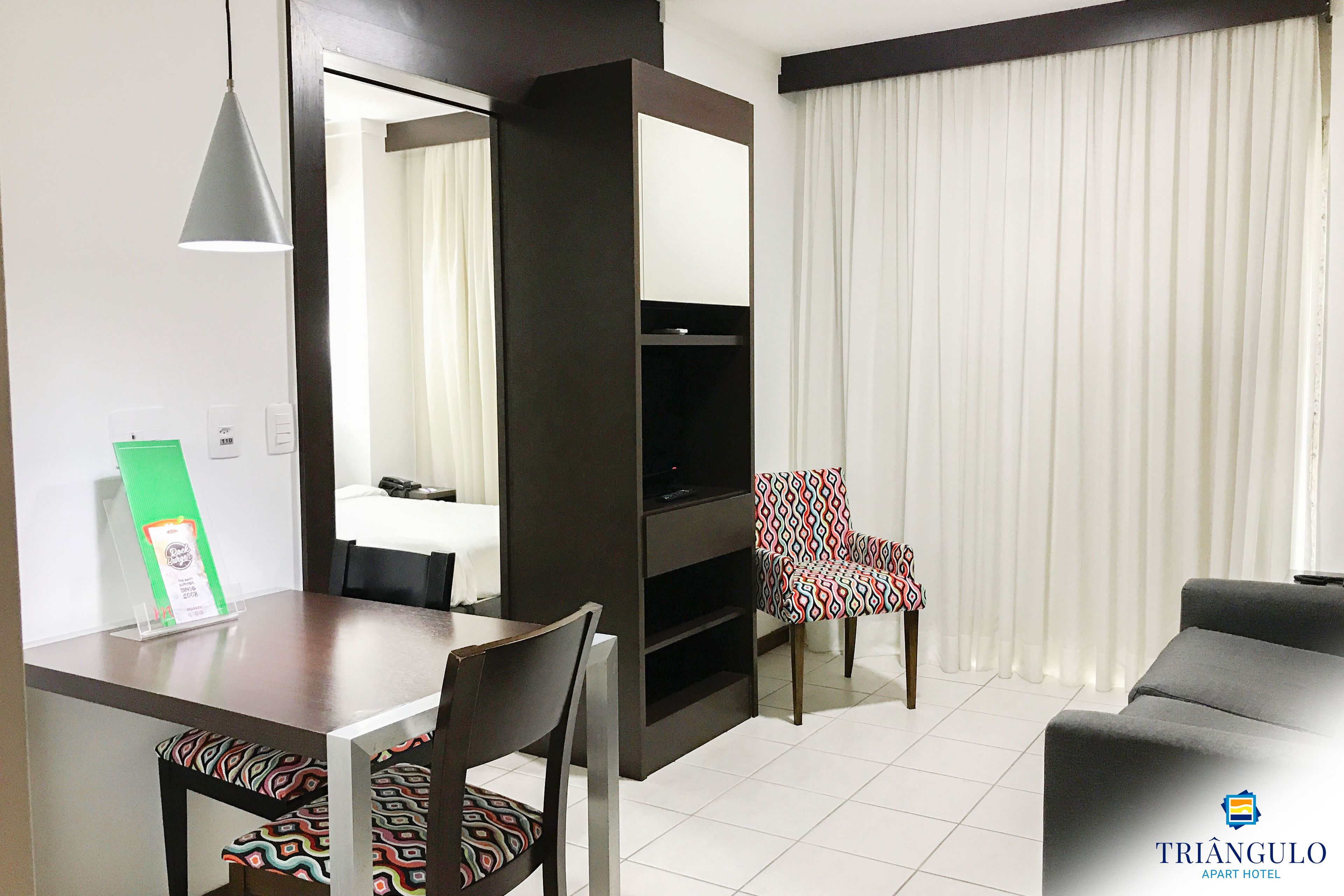 Una habitación de hotel moderna con zona de comedor, televisor y una silla estampada.