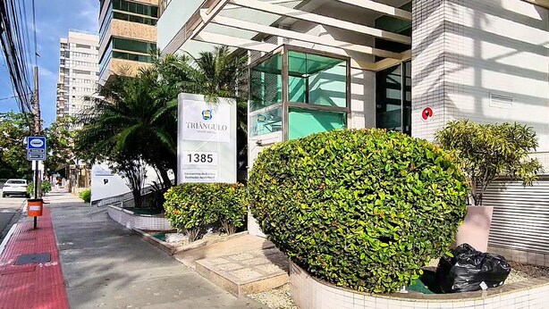 A modern building with a sign for Triangulo Apart Hotel at 1385, featuring a glass facade and a well-maintained hedge. - Triângulo Apart Hotel (Vitoria)