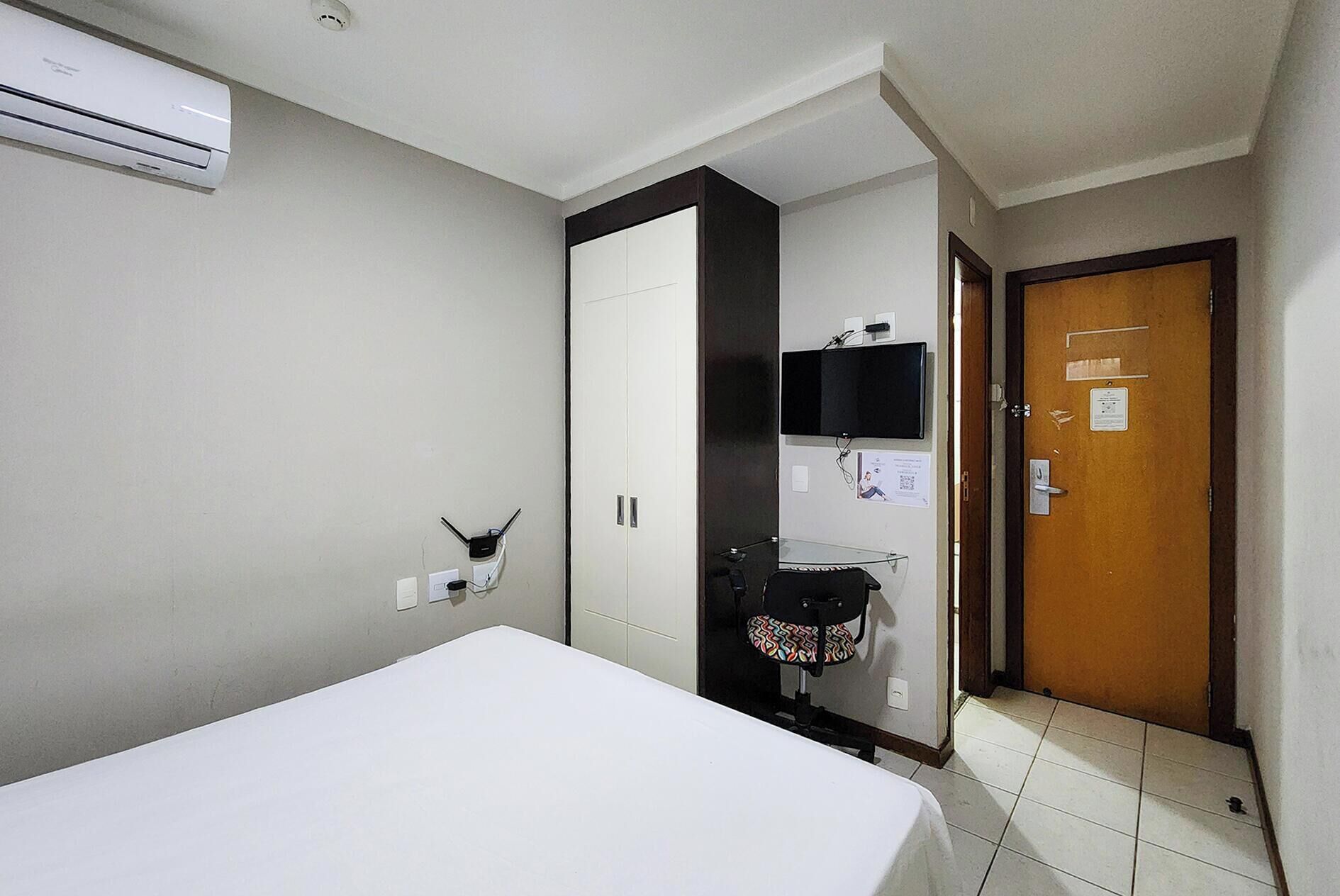 Una habitación de hotel con cama, armario, escritorio con silla, televisión y una puerta.