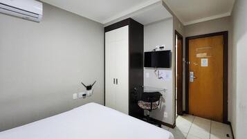 Una habitación de hotel con cama, armario, escritorio con silla, televisión y una puerta.
