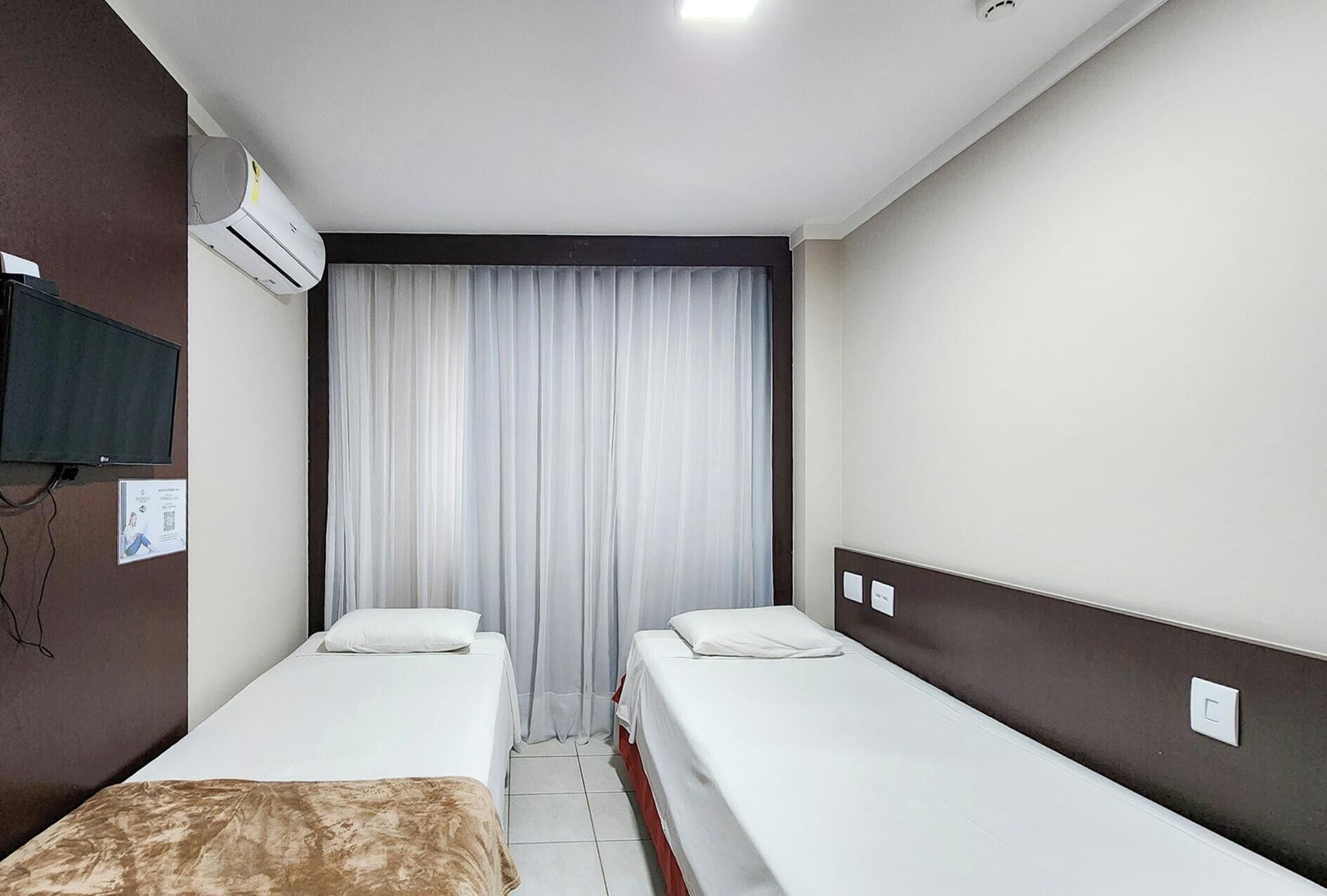 Una habitación de hotel con dos camas individuales, un televisor de pantalla plana, un equipo de aire acondicionado y una cortina.