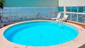 A rooftop pool with clear blue water, surrounded by a white railing and two white lounge chairs. - Triângulo Apart Hotel (Vitoria)