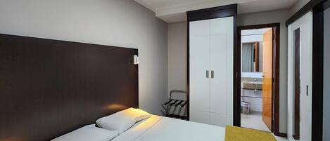Habitación de hotel con cama, armario, baño visible a través de una puerta abierta y una mesita con una silla.