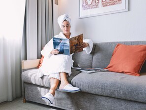 A person sitting on a grey sofa with an orange pillow, reading a book. - Novotel Venezia Mestre Castellana (Mestre)