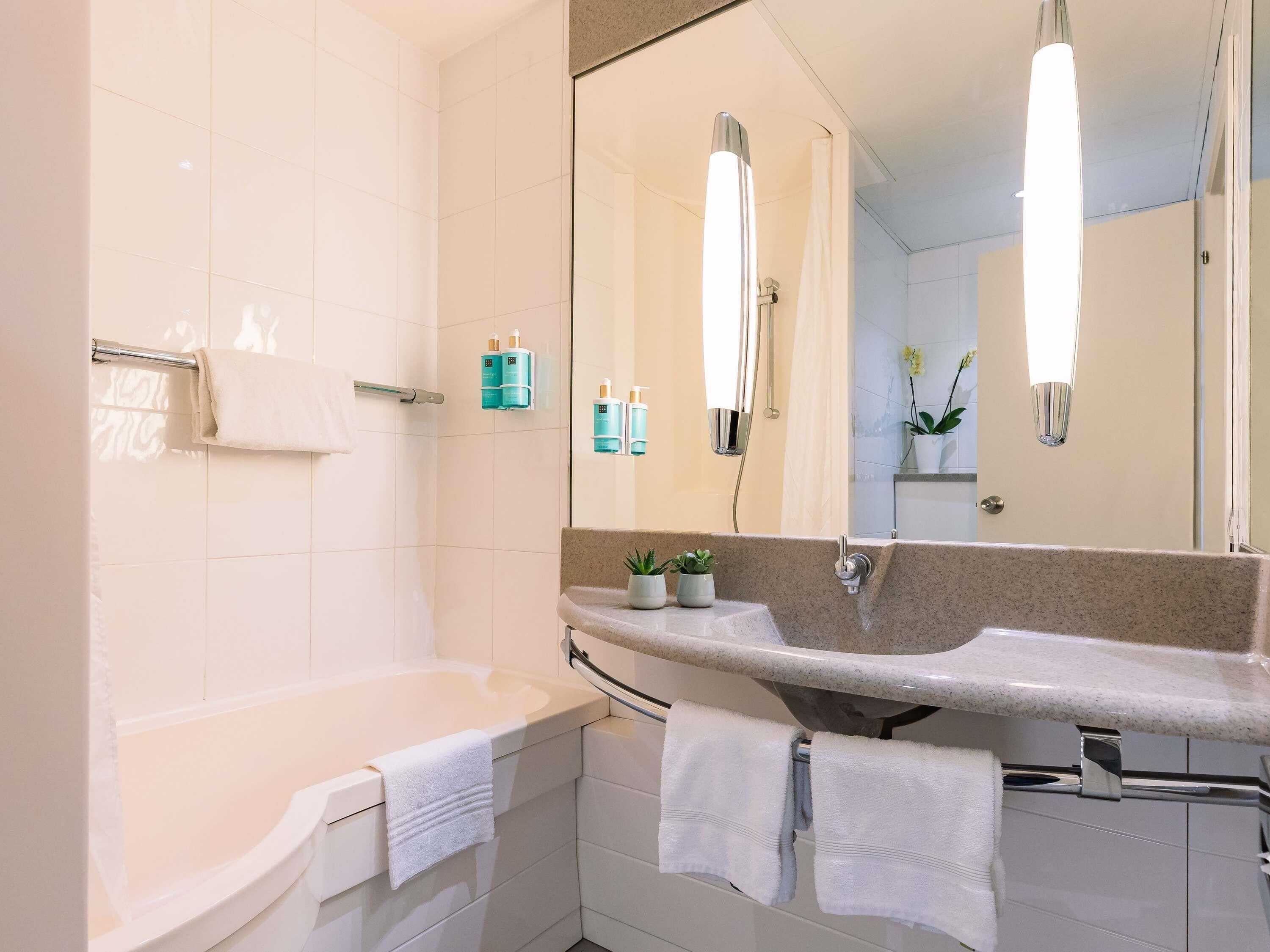 A modern bathroom with a bathtub, a large mirror, and a vanity with a sink and towel rack.