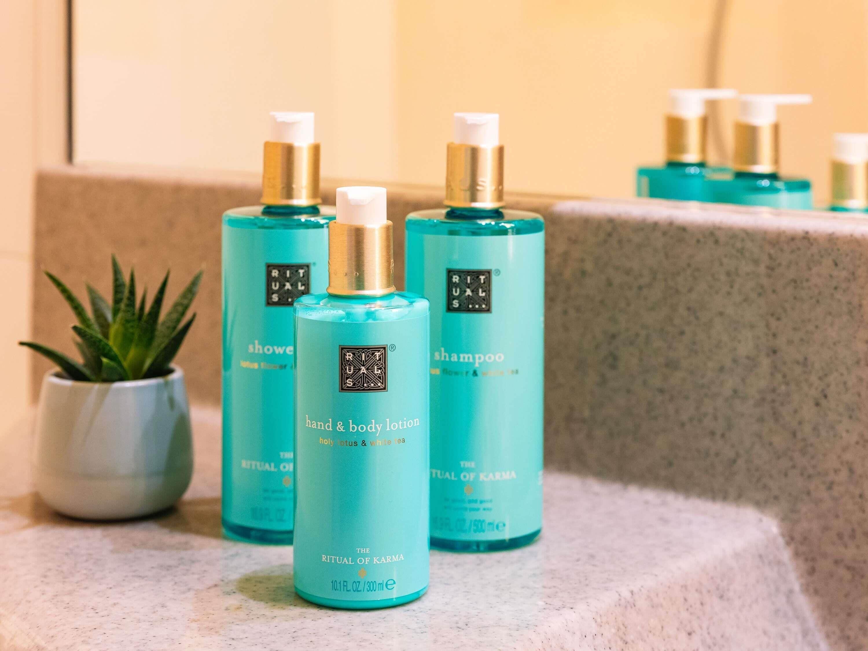 A bathroom counter with multiple bottles of hand and body lotion, a small potted plant, and a mirror reflecting the bottles.