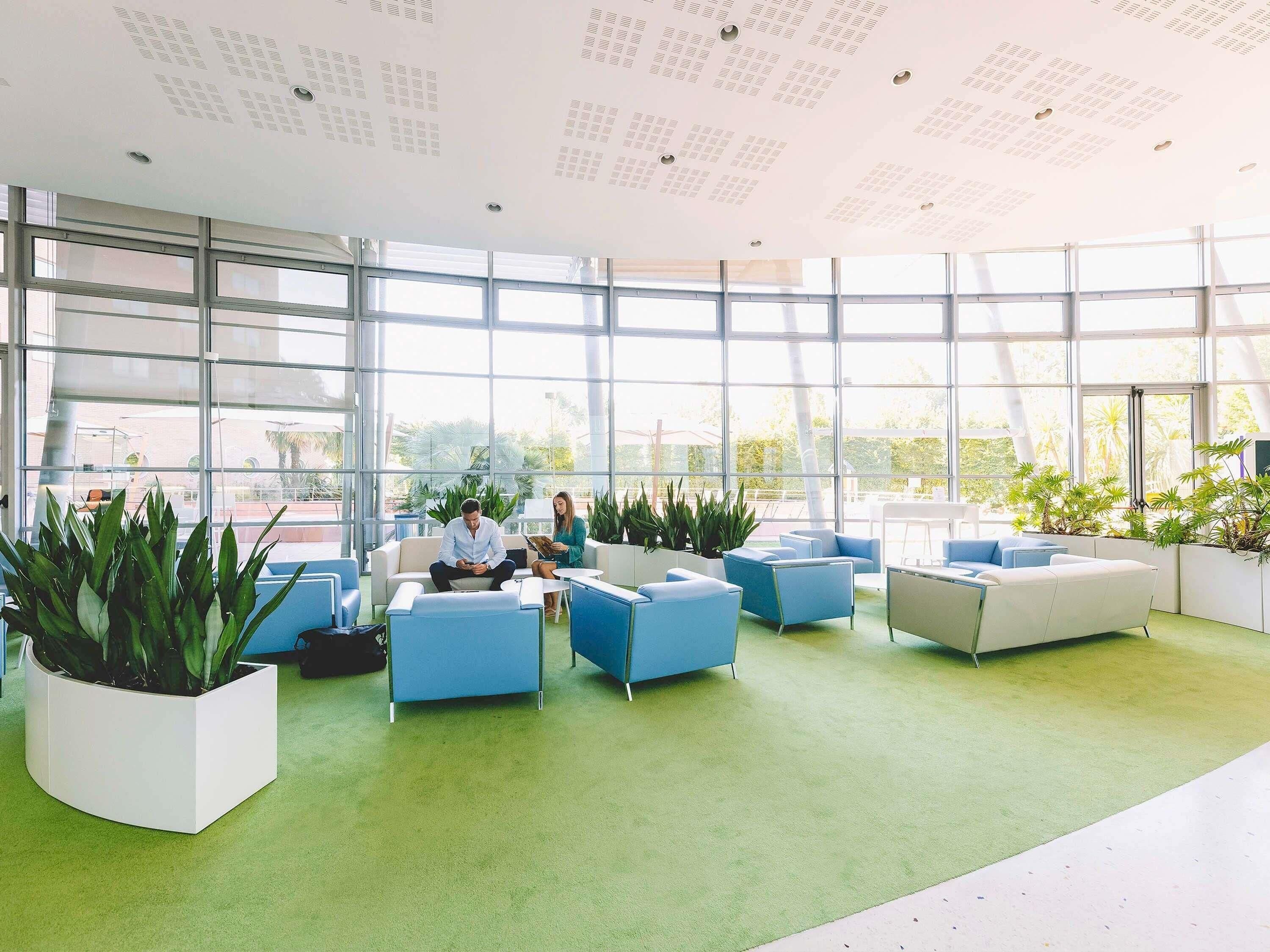 Un espace intérieur vaste et lumineux, avec de grandes fenêtres, une moquette verte et des sièges modernes.
