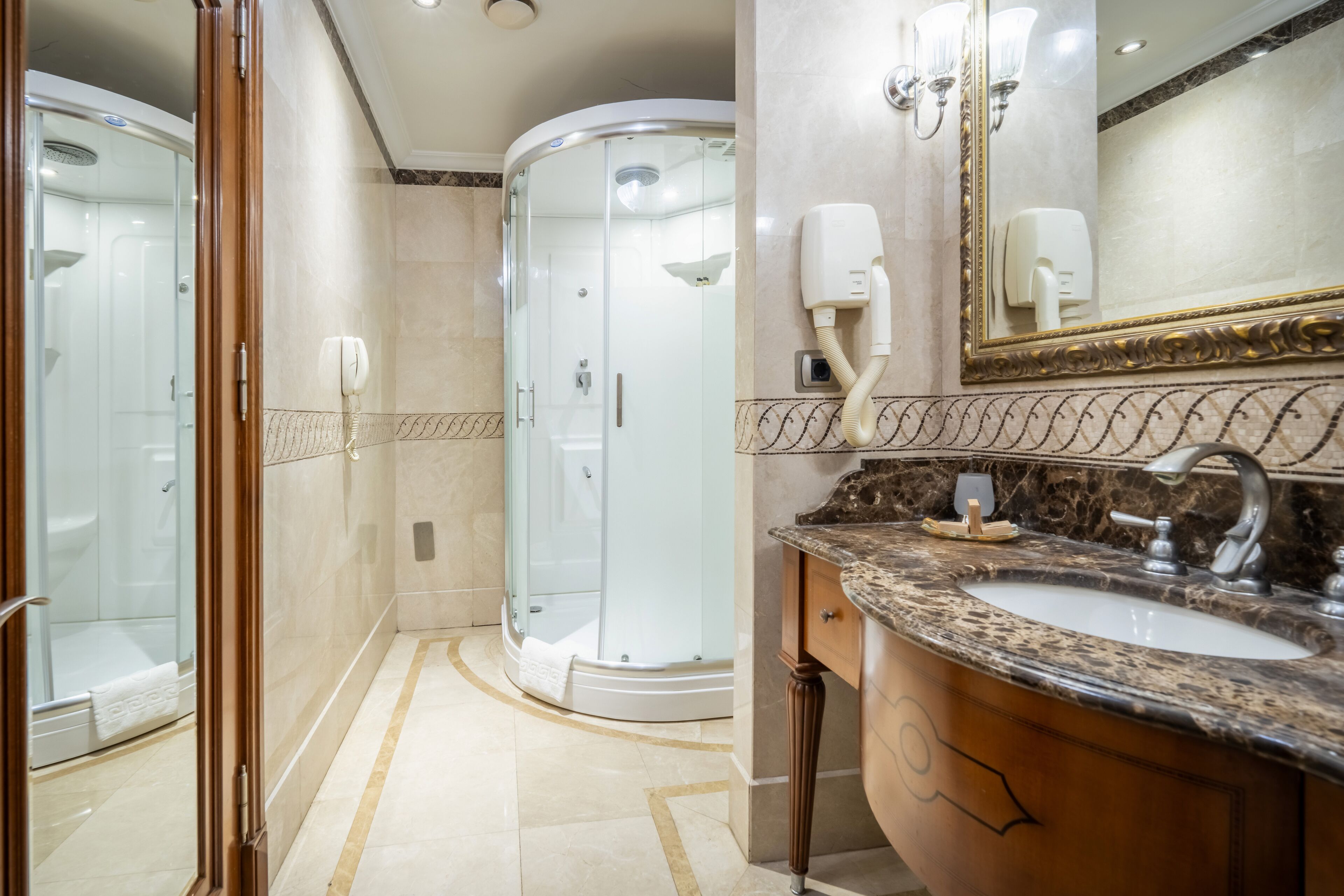 Une salle de bain moderne avec une douche à parois de verre, un lavabo en marbre et un grand miroir avec un cadre doré.