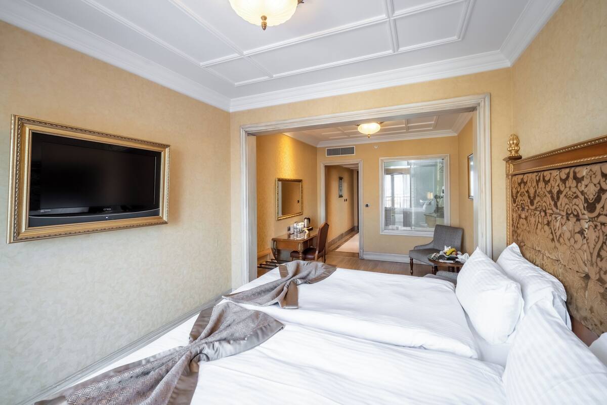 A hotel room with a large bed, a television mounted on the wall, a desk with a chair, and a mirror.