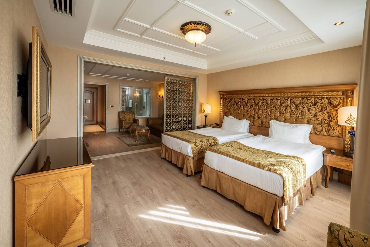 A hotel room with two beds, a wooden headboard, a nightstand, a TV, and a large mirror.