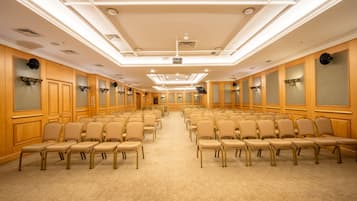 A conference room with rows of beige chairs, wooden paneling, and recessed ceiling lighting.