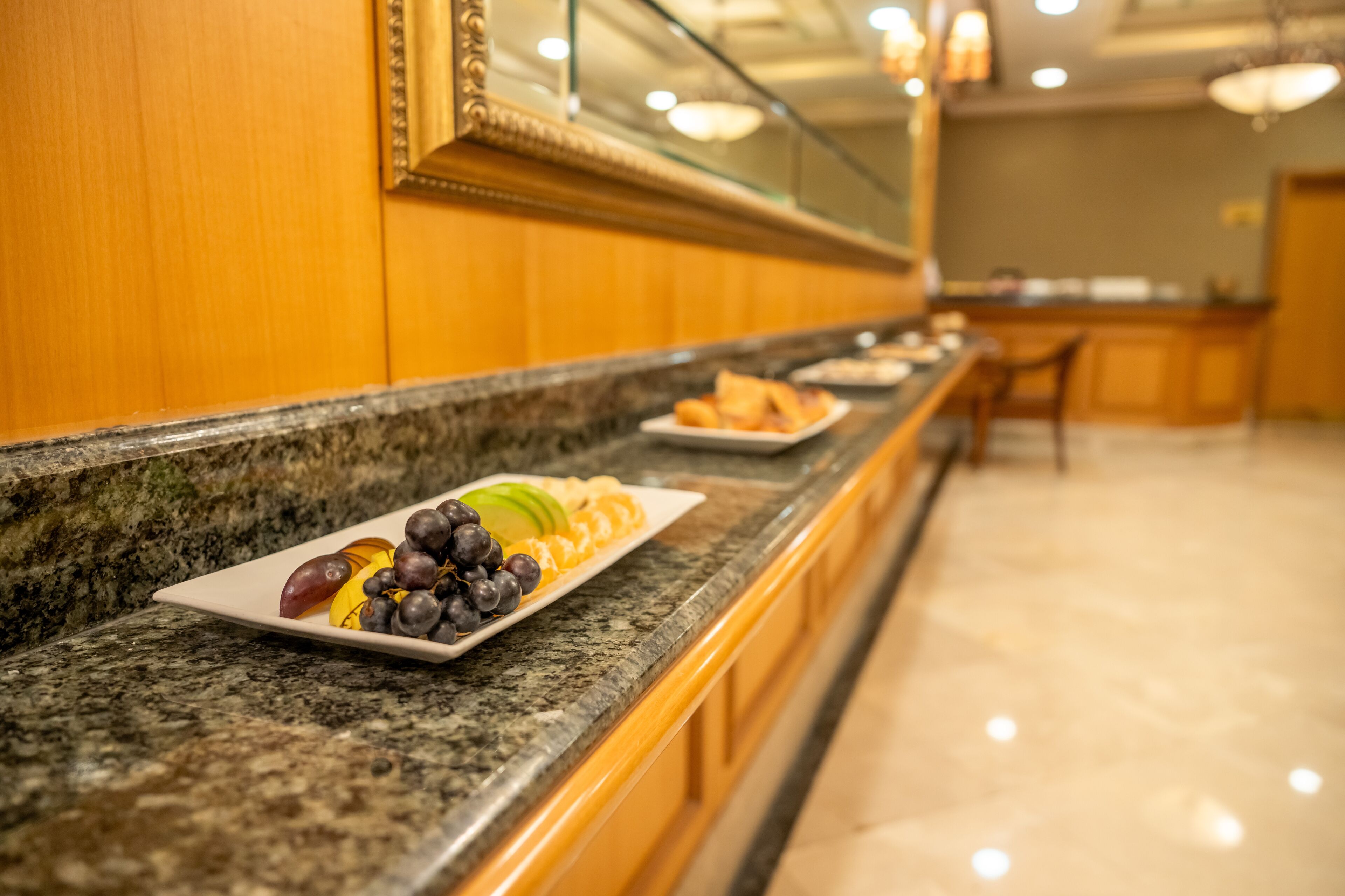 Un bufé de hotel con encimera de mármol, un plato de frutas y un espejo sobre la encimera.