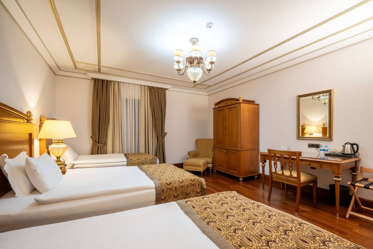 A hotel room with two beds, a desk, a wardrobe, and a chandelier.