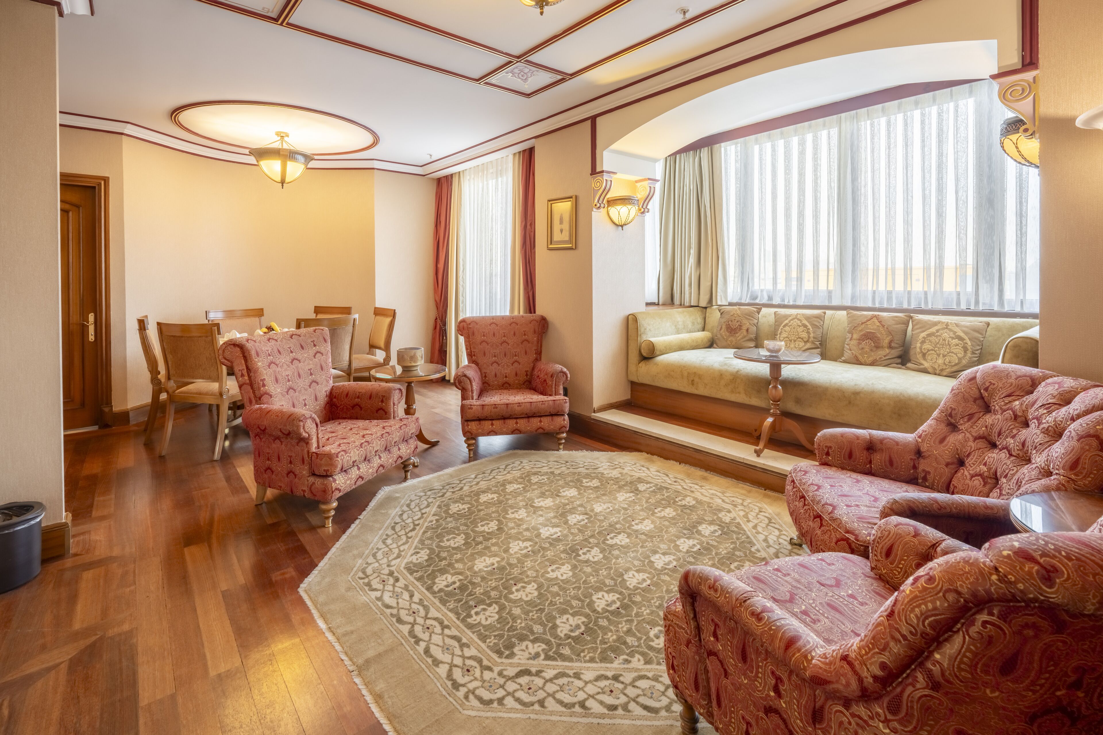 Uma sala de estar ampla, com um sofá grande, poltronas estampadas, uma mesa de centro e um espaço de jantar com cadeiras e mesa.
