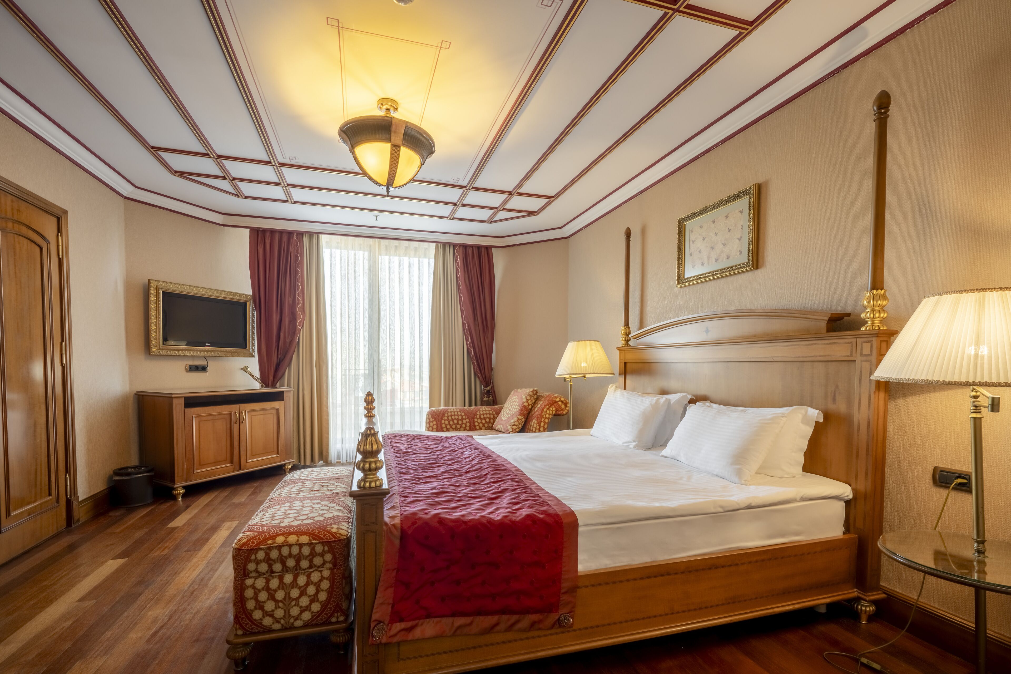 A hotel room with a large bed, a wooden wardrobe, a television, and a desk.