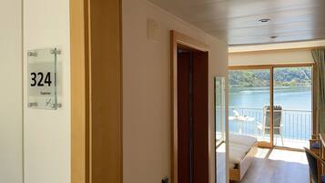 A hotel room with a balcony overlooking a lake, a bed, and a door with a room number sign.