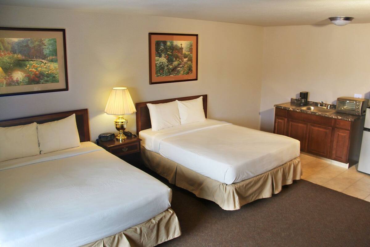 Quarto de hotel com duas camas, uma kitchenette pequena e um quadro na parede.