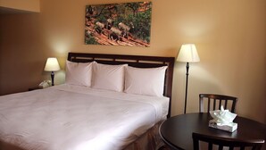 A hotel room with a large bed, two bedside lamps, a round table with a chair, and a painting on the wall. - The Inn at St George (St. George)