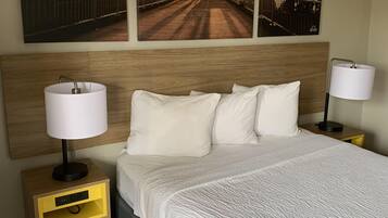Une chambre d’hôtel avec un grand lit, deux tables de chevet avec des lampes, une tête de lit en bois et trois tableaux encadrés représentant un pont, accrochés au mur.
