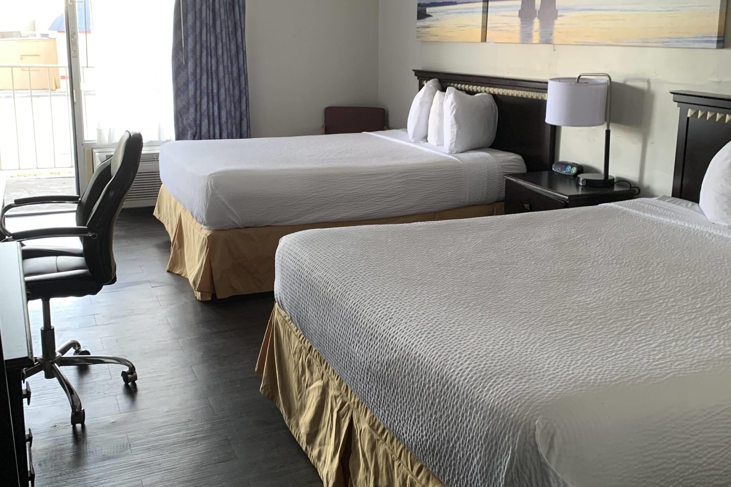 A hotel room with two beds, a desk, and a chair.