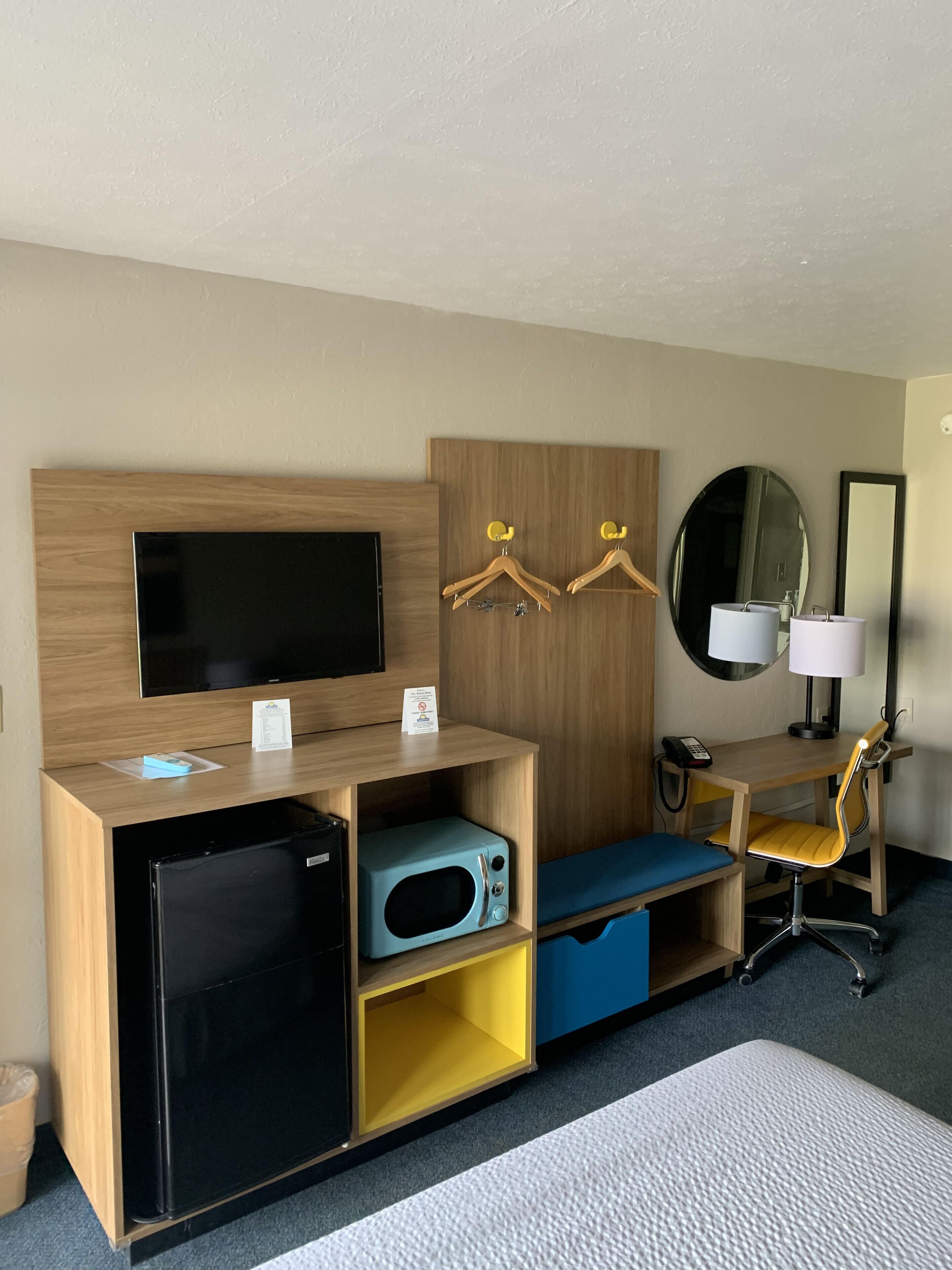 Een hotelkamer met een flatscreen-tv, een minibar, een magnetron, een bureau met stoel, een spiegel en een lamp.