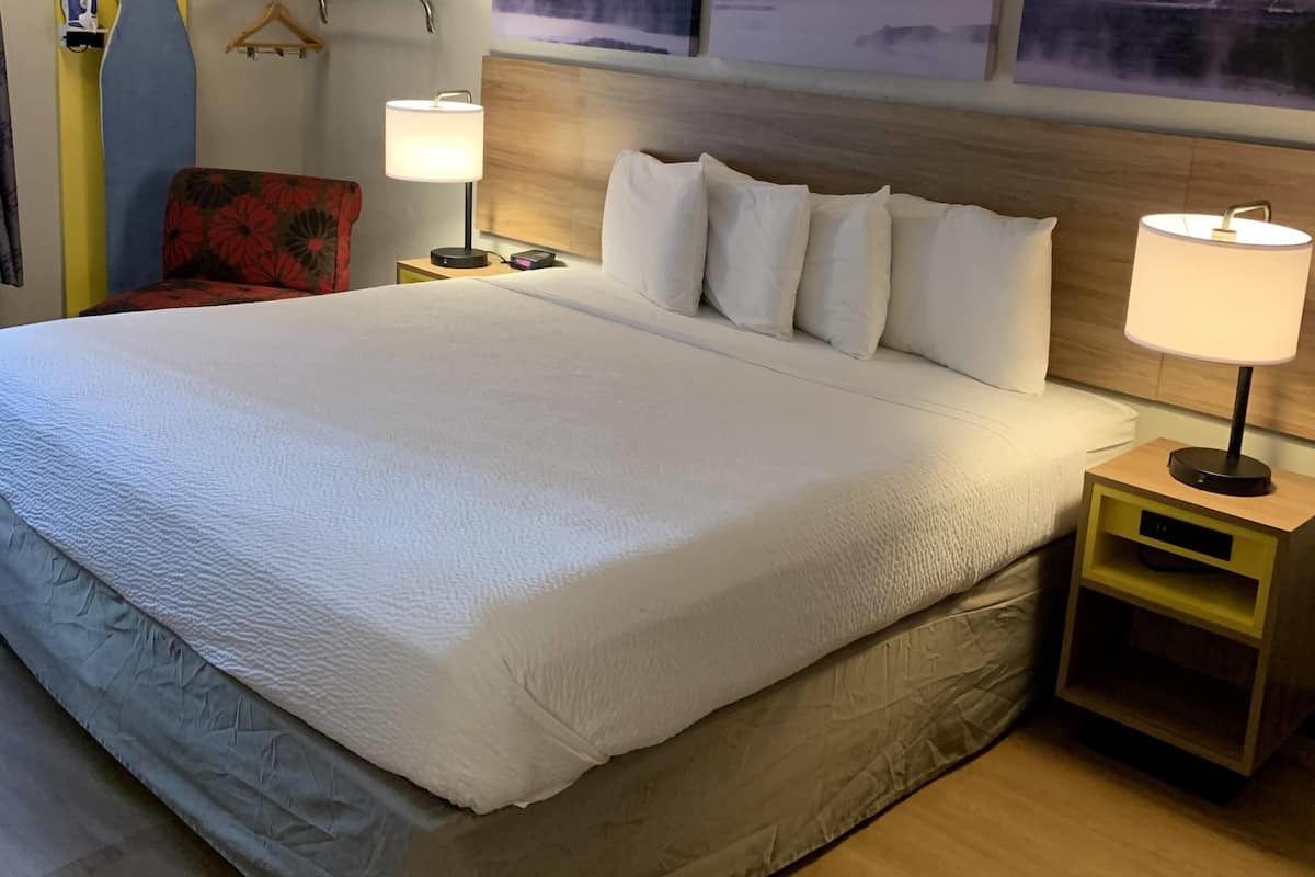 Une chambre d’hôtel avec un grand lit, deux tables de chevet avec des lampes, une chaise et une tête de lit en bois.