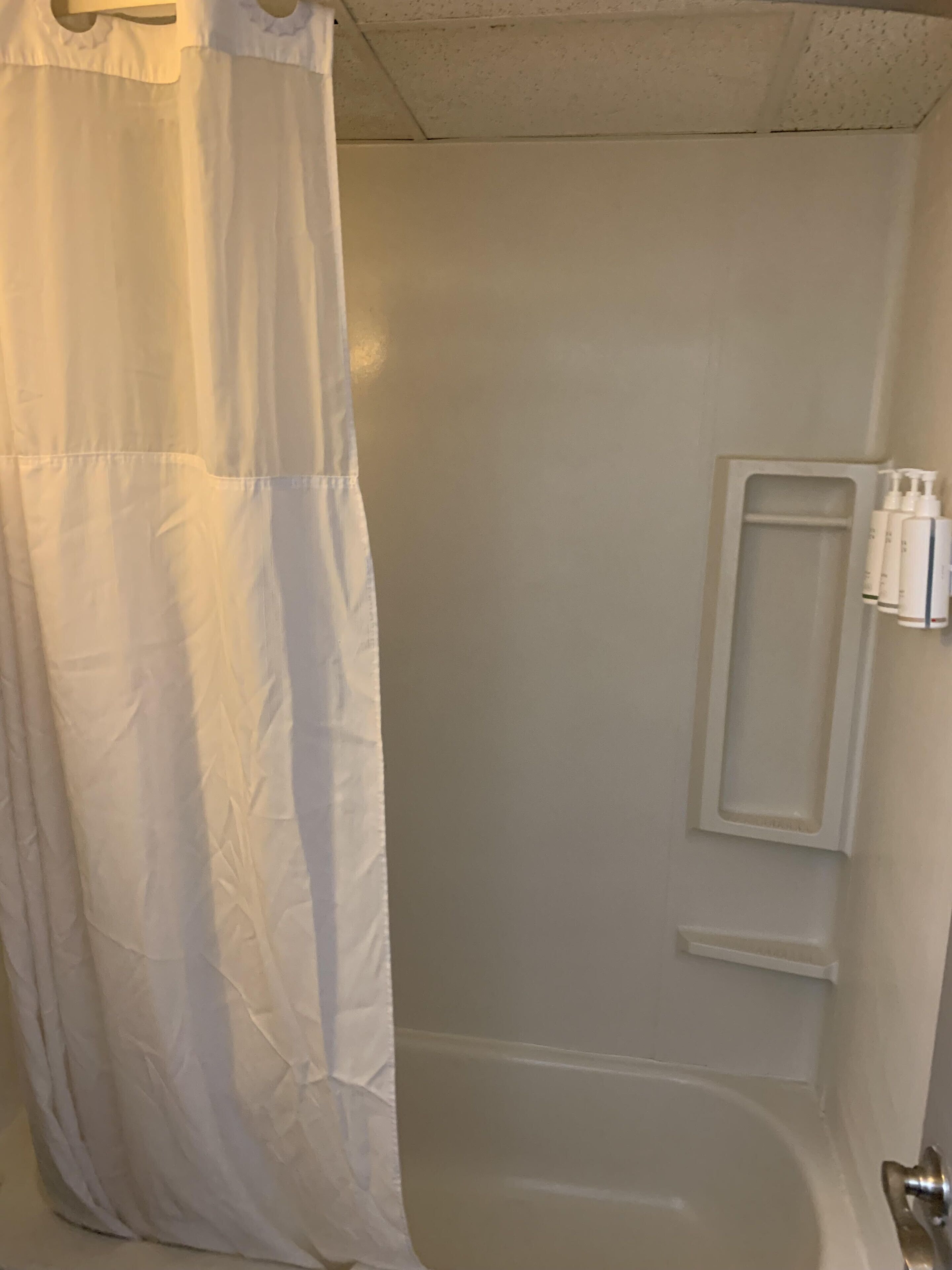 A bathroom with a white bathtub, a shower curtain, and a shelf with toiletries.