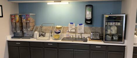 A breakfast bar with cereal dispensers, a coffee machine, a toaster, and a refrigerator with milk cartons.