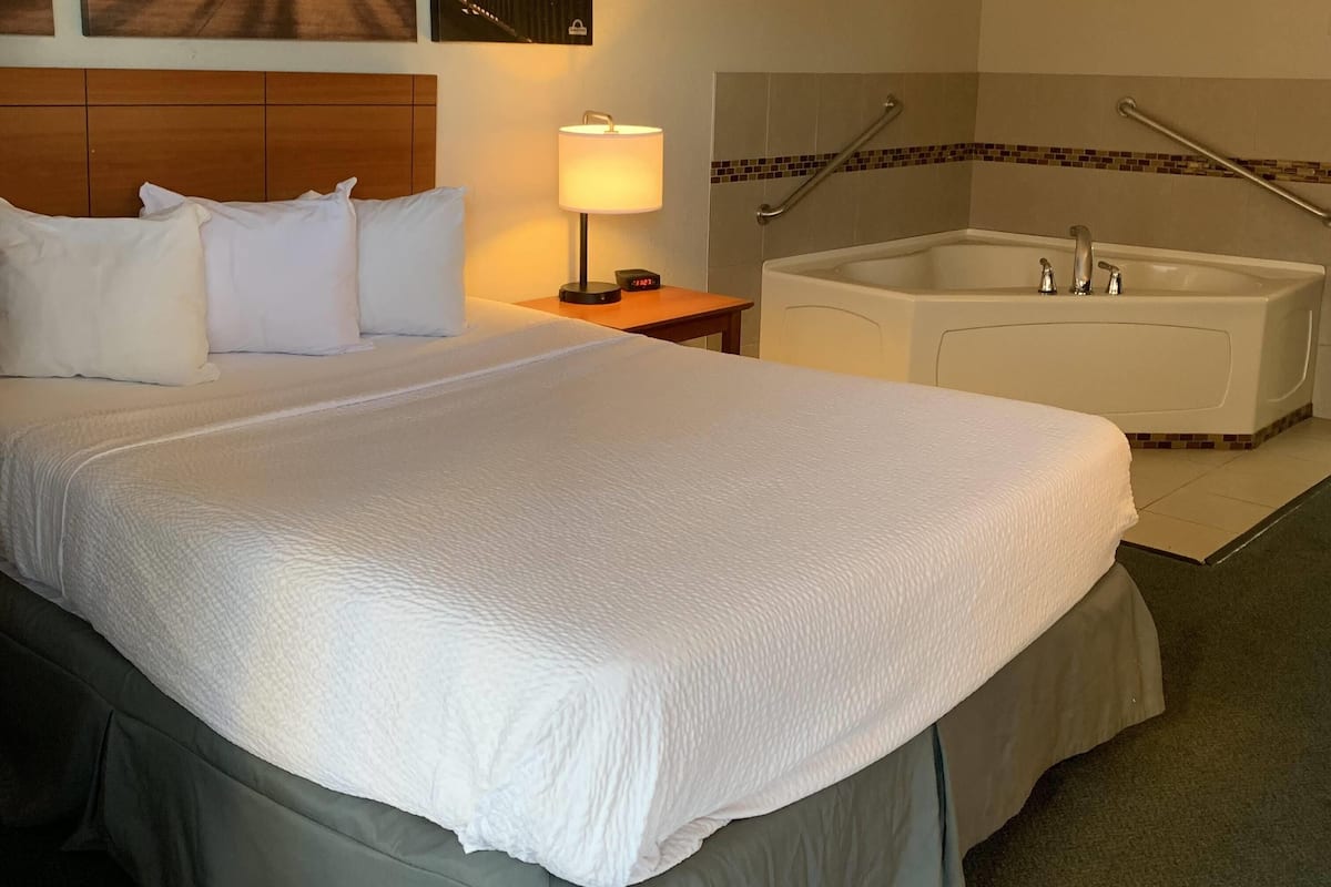 Une chambre d’hôtel avec un grand lit, une lampe de chevet, une baignoire intégrée et une tête de lit en bois.