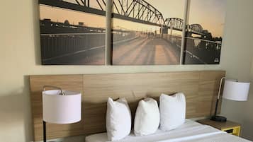 A hotel room with a large bed, two bedside tables with lamps, a wooden headboard, and three framed pictures of a bridge on the wall.