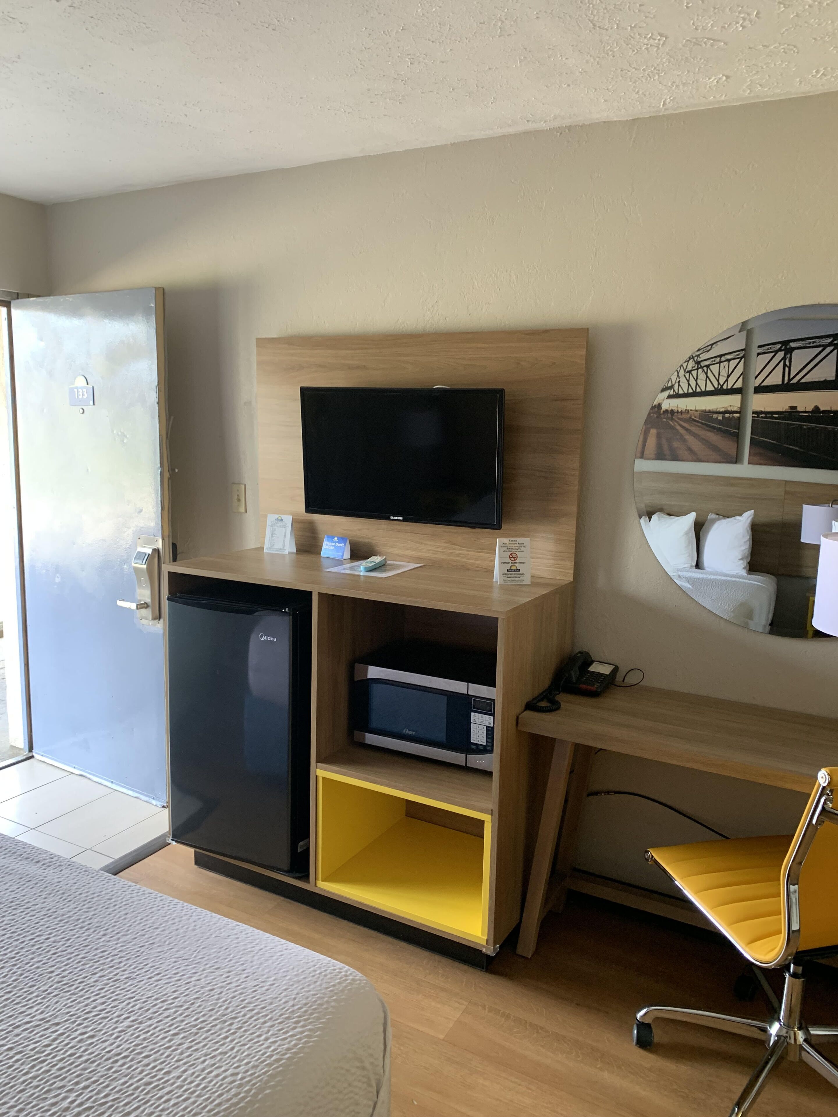 Une chambre d’hôtel équipée d’un lit, d’un bureau avec un ordinateur, d’une télévision, d’un mini-bar et d’un miroir.